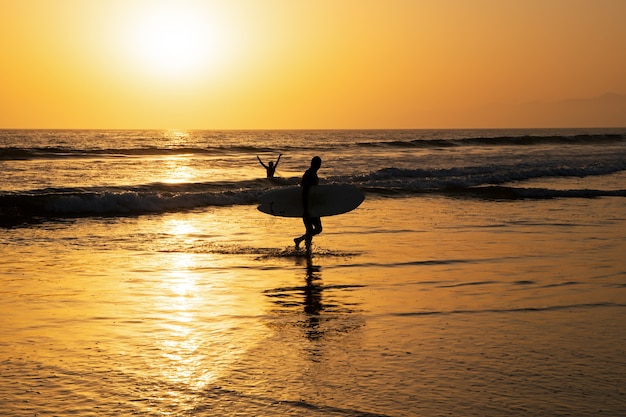 Surfen bei Sonnenuntergang. Mann mit Surfbrett. Aktiver Lebensstil der Menschen im Freien.