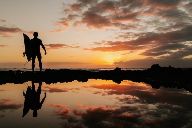 Surfen bei Sonnenuntergang mit Spiegelung des Himmels auf dem Wasser