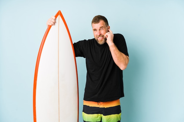 Foto surfen hombre aislado en la pared azul que cubre los oídos con las manos.