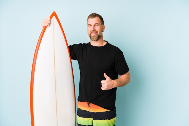 Surfen homem isolado na parede azul, sorrindo e levantando o polegar