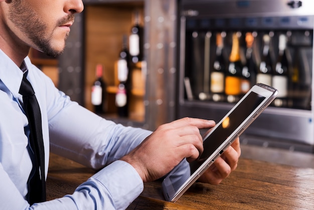 Surfen im Internet in der Bar. Nahaufnahme eines Mannes in Hemd und Krawatte, der an einem digitalen Tablet arbeitet, während er an der Bartheke sitzt