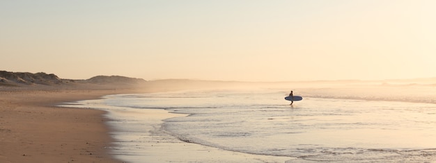 Surfer corriendo en la playa al amanecer.