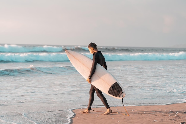 Surfer, der am Strand mit einem Surfbrett ins Meer geht