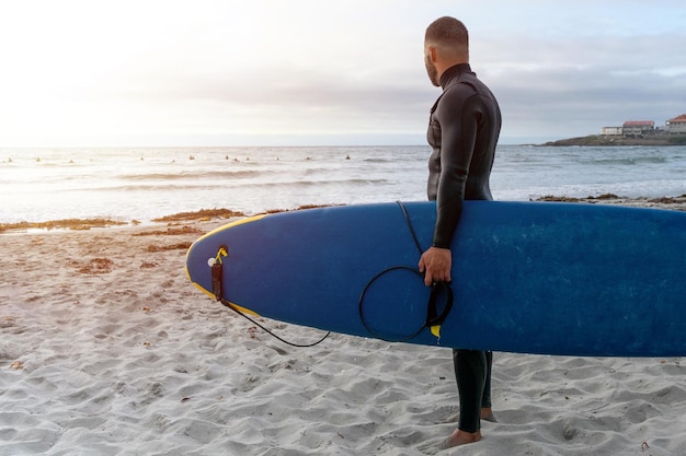 Surfer, der das Surfbrett trägt, während er andere Surfer anschaut, bevor er zum Surfen ins Meer geht