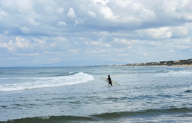 Surfer mit dem Neoprenanzug, der mit seinem Surfbrett im blauen Meer taucht