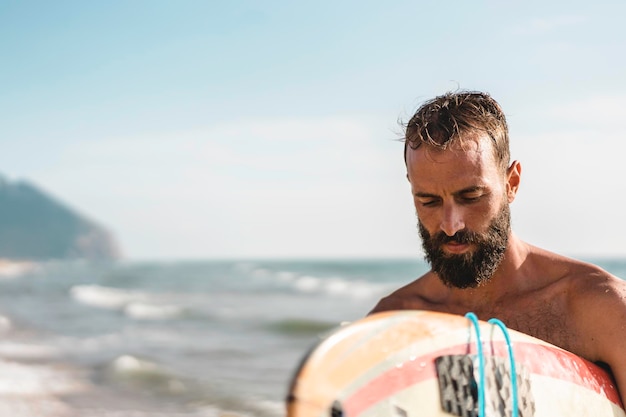Surfer sosteniendo su tabla de surf caminando en la playa Hombre hipster entrenando con tabla de surf Concepto de estilo de vida y libertad