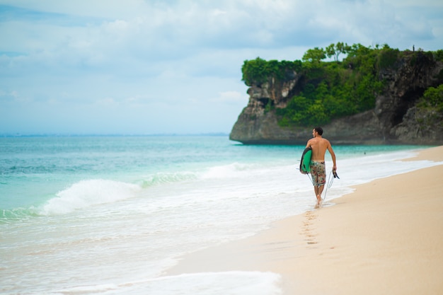 Surfer. Surfing Man With Surfboard Walking auf tropischem Sandstrand.