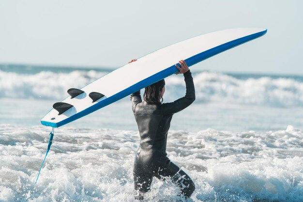 Surferfrau geht mit dem Surfbrett auf dem Kopf in Richtung der Wellenrückansicht