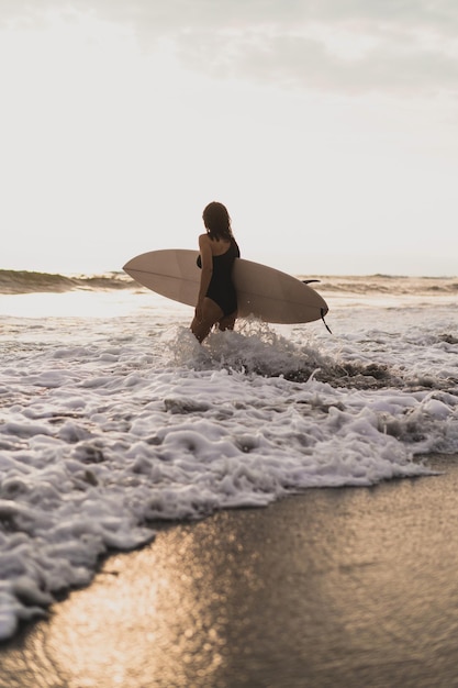 Surferin mit Surfbrett auf dem Meer bei Sonnenuntergang