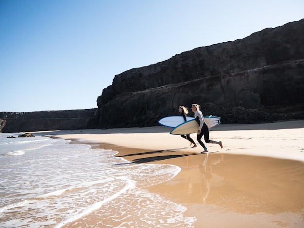 Surferinnen am Strandufer, die zu den Wellen laufen