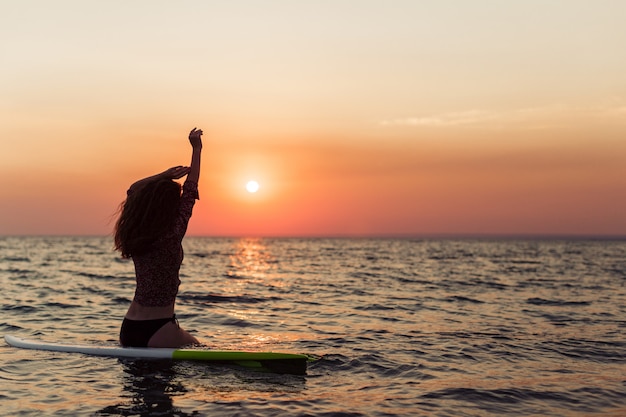 Surfermädchen, das Ozeanstrandsonnenuntergang betrachtend surft