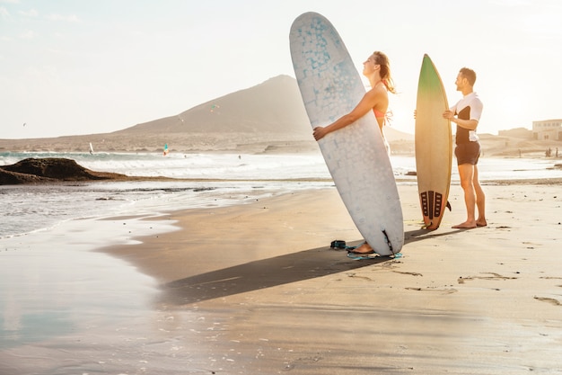 Surferpaar wartet auf die hohen Wellen am Strand - Sportliche Menschen mit Surfbrettern bei Sonnenuntergang - Extremsport- und Urlaubskonzept - Fokus auf weibliches Gesicht