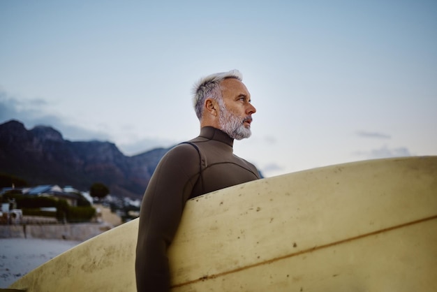 Surferstrand und alter Mann mit Surfbrett, um mit Freiheit und Meereswellen in Brasilien im Freien zu surfen Sporttourist und Senior im Ruhestand mit Blick auf Meerwasser im Urlaub