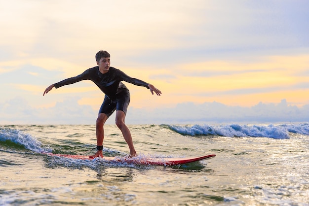 Surfista adolescente surfando ondas em prancha macia na praia de Rayong, Tailândia Estudante de prancha de surf adolescente novato jogando na água em ação animada e engraçada
