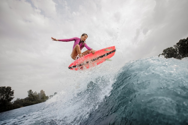 Surfista ativo e jovem mulher pulando a onda azul contra o céu