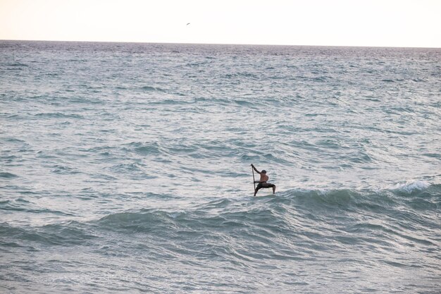 Surfista atlético con alambre nada con una paleta en una tabla de apoyo en el mar Stand up paddleboarding