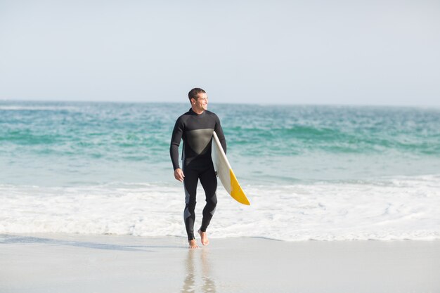 Surfista caminando por la playa con una tabla de surf