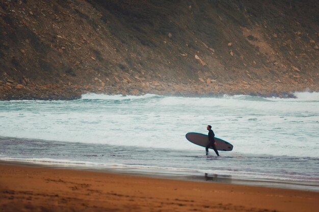 Foto un surfista está caminando por la playa con una tabla de surf