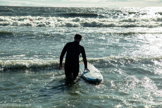 Surfista entra no mar ao pôr do sol