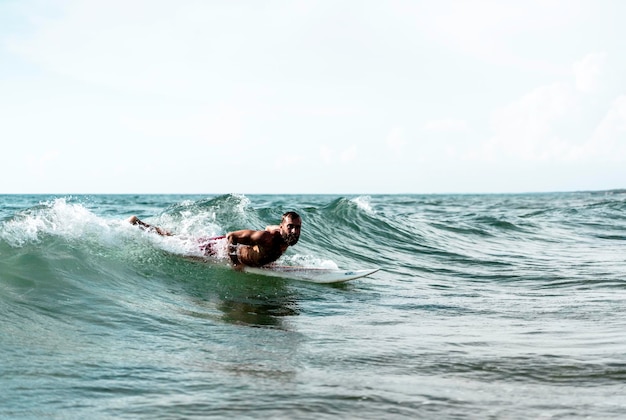 Surfista hipster escorregando nas ondas deitado em sua prancha com uma grande onda no mar Homem barbudo treinando com prancha de surf para o mar Conceito de aventura e liberdade fazendo esportes radicais aquáticos