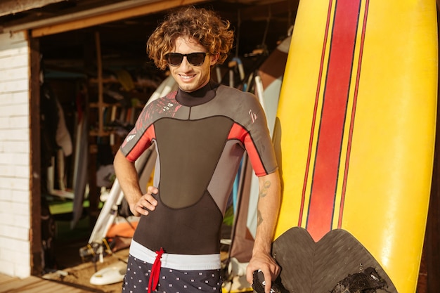 Surfista jovem feliz com óculos de sol em pé na praia