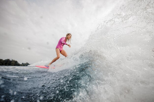 Surfista loira jovem descendo a onda azul espirrando