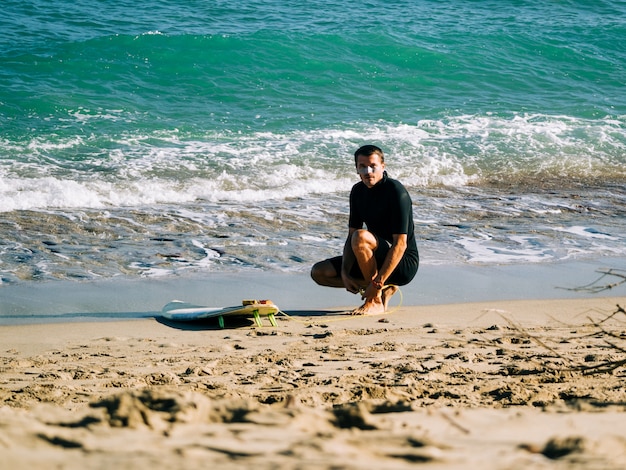 Surfista masculino amarrando a trela da prancha na perna na praia. Oceano Atlântico.