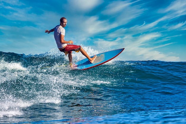 Surfista masculino en una ola azul en un día soleado