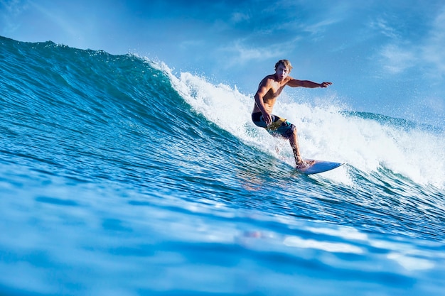 Surfista masculino en una ola azul en un día soleado