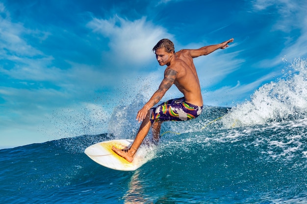 Surfista masculino en una ola azul en un día soleado