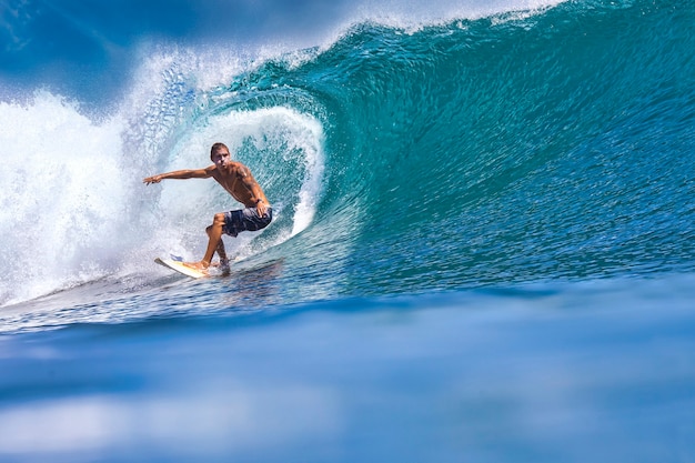 Surfista masculino en una ola azul en un día soleado