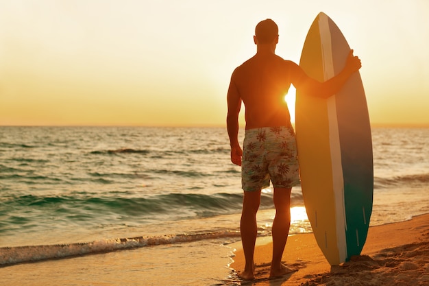 Surfista na praia do oceano ao pôr do sol