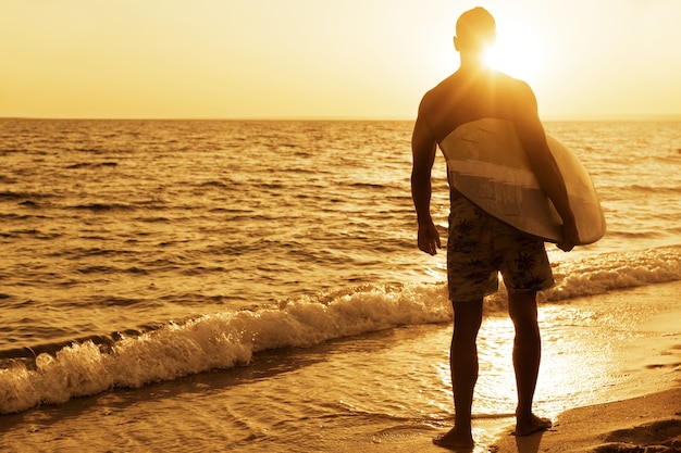 Foto surfista na praia do oceano ao pôr do sol