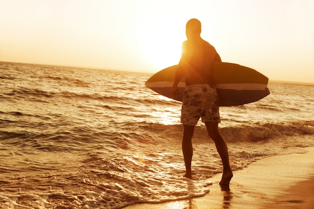 Surfista na praia do oceano ao pôr do sol