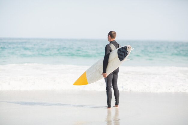 Surfista de pie en la playa con una tabla de surf