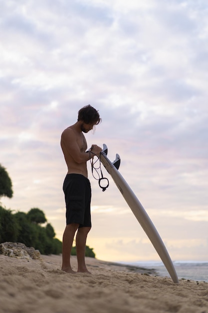 Surfista sexy surfista con tabla de surf. Un apuesto joven atleta sosteniendo una tabla de surf con el pelo mojado en unas vacaciones deportivas en la playa de verano. Destino de viajes deportivos. Estilo de vida de surf.