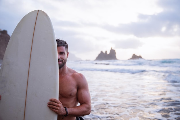 Surfista sonriente cubre la mitad de su rostro con tabla de surf deportes extremos y concepto de felicidad