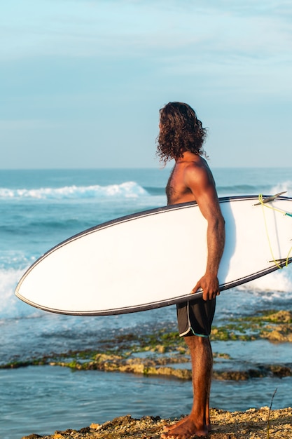 El surfista sostiene una tabla de surf en la orilla del Océano Índico