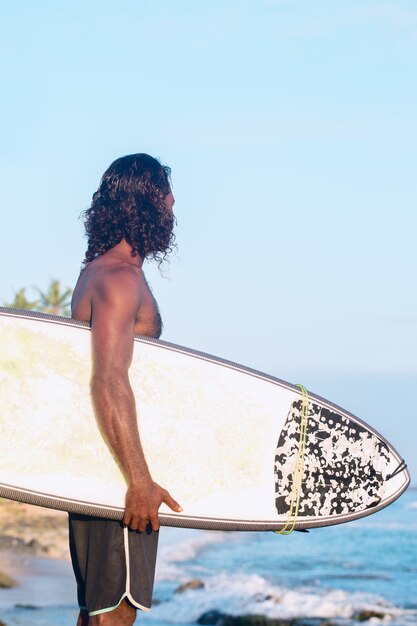 El surfista sostiene una tabla de surf en la orilla del Océano Índico