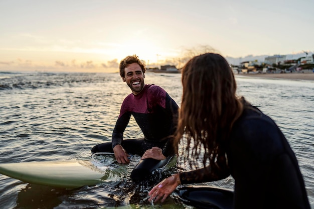 Surfistas felices sentados en tablas en el agua y sonriendo el uno al otro