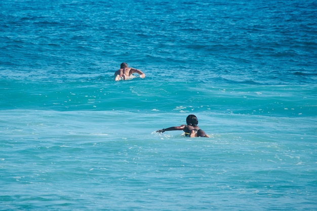 Los surfistas de hombre blanco y mujer negra nadan en línea. Vista trasera. Lifestule