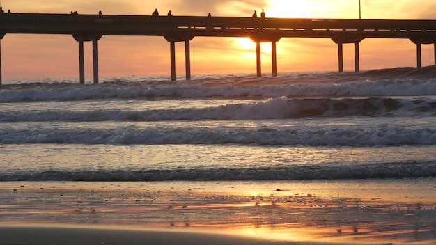 Surfistas surfando por ondas de água oceânicas de cais pessoas e céu ao pôr do sol na califórnia