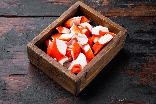 Surimi aus frischem Krabbenfleisch mit blauem Schwimmkrabbenset in Holzkiste auf dunklem Holztisch