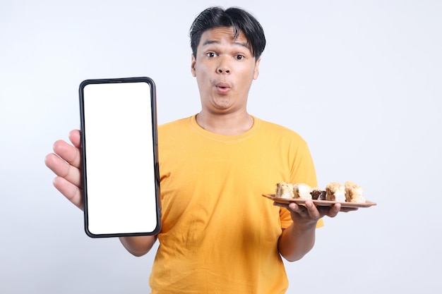 Surpreenda um jovem asiático mostrando uma grande tela de telefone em branco para uma maquete enquanto segura sushi em uma bandeja de madeira