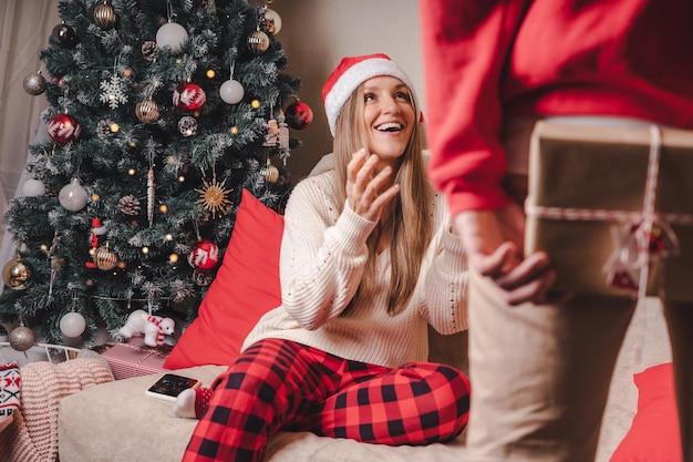 Surpreendendo a vista traseira em close de um homem de suéter vermelho segurando uma caixa de presente de Natal atrás da dele