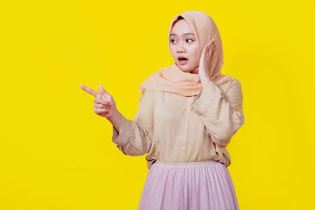 Foto surpreendente mulher asiática usando hijab com o dedo apontando isolado no fundo do banner amarelo claro