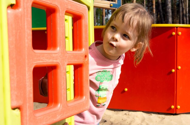 Foto surpreendida criança feliz espreitando para fora de uma pequena casa no playground brincar de esconde-esconde