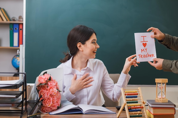 surpreendida jovem professora recebeu cartão postal sentado na mesa com ferramentas escolares em sala de aula