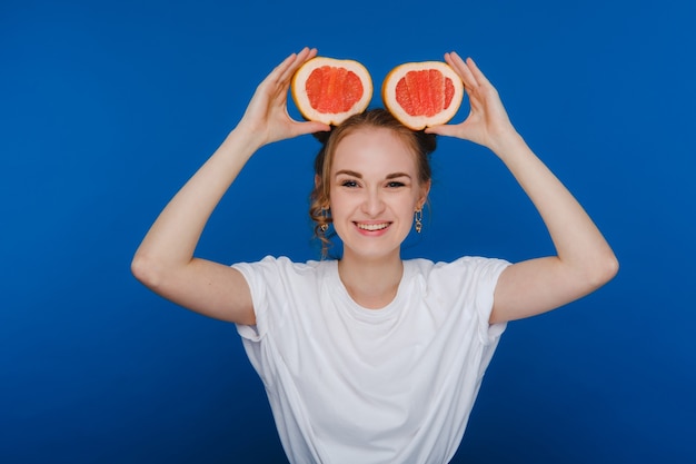 Surpresa, a garota sorridente segura a toranja como orelhas. Estilo de vida vegano. Mulher sorridente, comendo o conceito. Dieta orgânica, perda de peso e alimentação saudável. Smoothies e sucos naturais.