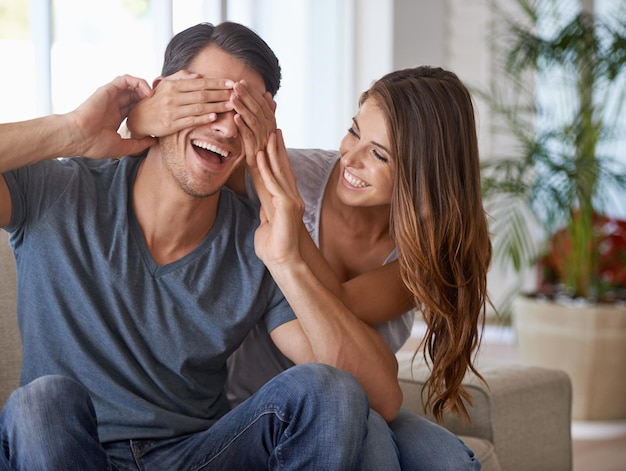 Surpresa de casal e mãos cobrem os olhos para uma revelação feliz na sala de estar de casa ou mulher sentada junto com parceiro e sofá Namorada homem e amor ou brincando de adivinhar quem ou anúncio animado